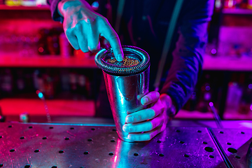 Image showing Close up of barman finishes preparation of alcoholic cocktail with shaker in multicolored neon light