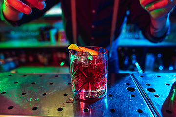 Image showing Close up of barman finishes preparation of alcoholic cocktail in multicolored neon light