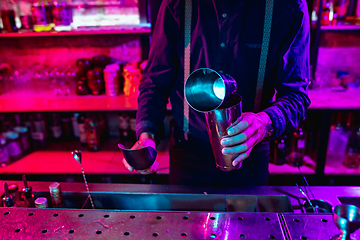 Image showing Close up of barman finishes preparation of alcoholic cocktail with shaker in multicolored neon light