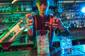 Image showing Barman finishes preparation of alcoholic cocktail with shot in multicolored neon light