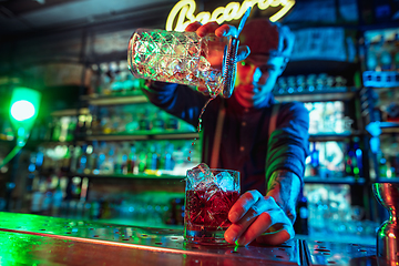 Image showing Close up of barman finishes preparation of alcoholic cocktail in multicolored neon light