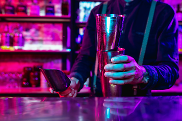 Image showing Close up of barman finishes preparation of alcoholic cocktail with shaker in multicolored neon light