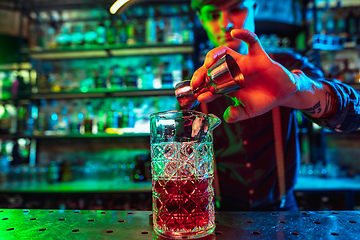 Image showing Barman finishes preparation of alcoholic cocktail with shot in multicolored neon light