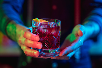 Image showing Close up of barman finishes preparation of alcoholic cocktail in multicolored neon light