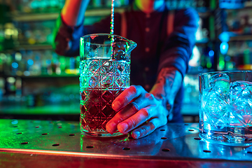 Image showing Close up of barman finishes preparation of alcoholic cocktail in multicolored neon light