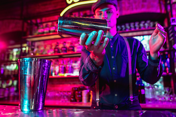 Image showing Barman finishes preparation of alcoholic cocktail with shaker in multicolored neon light