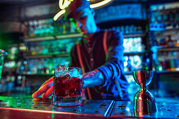 Image showing Close up of barman finishes preparation of alcoholic cocktail in multicolored neon light