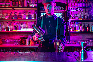 Image showing Barman finishes preparation of alcoholic cocktail with shaker in multicolored neon light