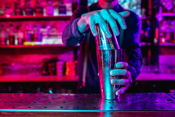 Image showing Close up of barman finishes preparation of alcoholic cocktail with shaker in multicolored neon light