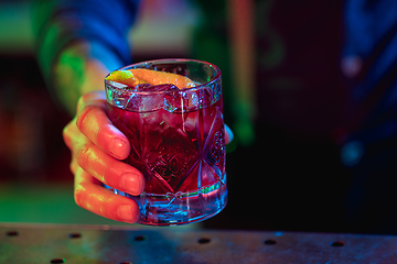 Image showing Close up of barman finishes preparation of alcoholic cocktail in multicolored neon light