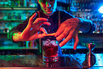 Image showing Close up of barman finishes preparation of alcoholic cocktail in multicolored neon light