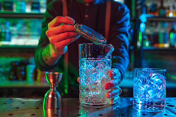 Image showing Close up of barman finishes preparation of alcoholic cocktail in multicolored neon light