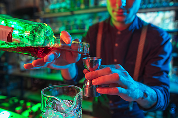 Image showing Barman finishes preparation of alcoholic cocktail with shot in multicolored neon light