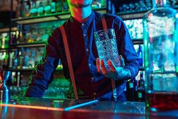 Image showing Close up of barman finishes preparation of alcoholic cocktail in multicolored neon light