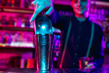 Image showing Close up of barman finishes preparation of alcoholic cocktail with shaker in multicolored neon light