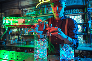 Image showing Barman finishes preparation of alcoholic cocktail with shot in multicolored neon light