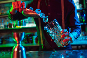 Image showing Close up of barman finishes preparation of alcoholic cocktail in multicolored neon light