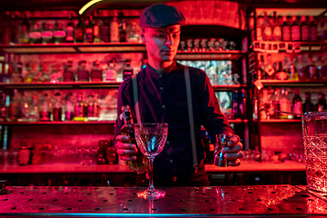 Image showing Barman preparing the alcoholic cocktail in multicolored neon light, focus on glass