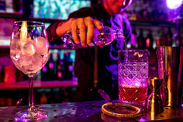 Image showing Close up of barman finishes preparation of alcoholic cocktail, pouring drink in multicolored neon light