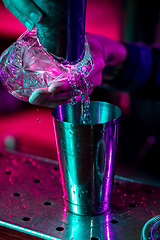 Image showing Close up of barman finishes preparation of alcoholic cocktail, pouring drink in multicolored neon light