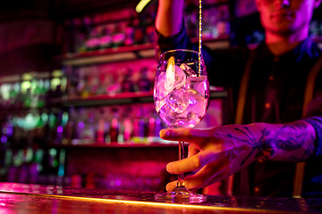 Image showing Close up of barman finishes preparation of alcoholic cocktail, pouring drink in multicolored neon light