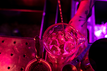 Image showing Close up of barman finishes preparation of alcoholic cocktail, shaking ice in multicolored neon light