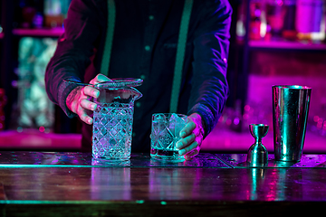 Image showing Close up of barman finishes preparation of alcoholic cocktail in multicolored neon light