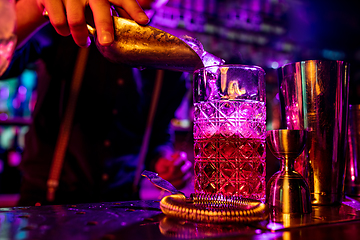 Image showing Close up of barman finishes preparation of alcoholic cocktail, pouring drink in multicolored neon light