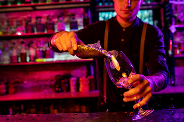 Image showing Close up of barman finishes preparation of alcoholic cocktail, pouring drink in multicolored neon light