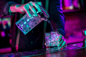 Image showing Close up of barman finishes preparation of alcoholic cocktail, pouring drink in multicolored neon light