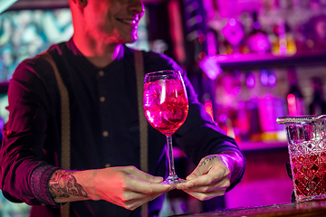 Image showing Barman proposing alcoholic cocktails, shots, beverages to guest in multicolored neon light