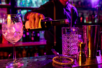 Image showing Close up of barman finishes preparation of alcoholic cocktail, pouring drink in multicolored neon light