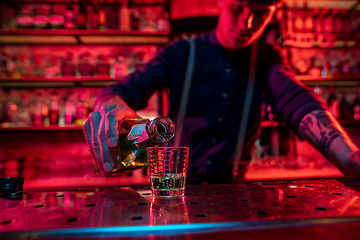 Image showing Barman finishes preparation of alcoholic cocktail, pouring drink in multicolored neon light, focus on glass