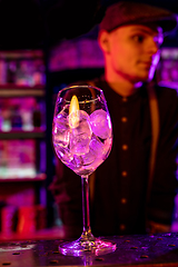 Image showing Barman finishes preparation of alcoholic cocktail in multicolored neon light, focus on glass