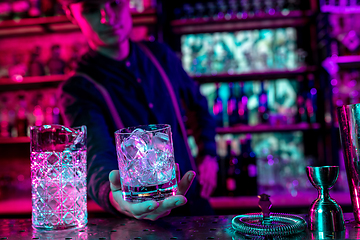 Image showing Close up of barman finishes preparation of alcoholic cocktail in multicolored neon light