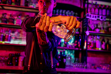 Image showing Close up of barman finishes preparation of alcoholic cocktail, shaking ice in multicolored neon light