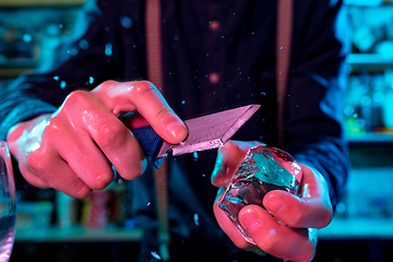 Image showing Close up of barman crushing a big piece of ice on the bar counter with a special bar equipment on it for a cocktail