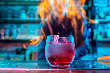 Image showing Close up of alcoholic cocktail, beverage, drink in multicolored neon light with fire flames on the background