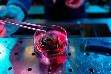 Image showing Close up of barman decorating, preparing of alcoholic cold cocktail in multicolored neon light