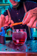 Image showing Close up of barman decorating, preparing of alcoholic cold cocktail in multicolored neon light