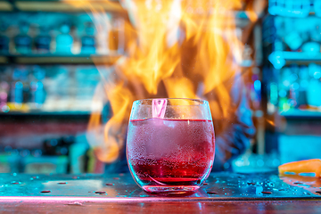 Image showing Close up of alcoholic cocktail, beverage, drink in multicolored neon light with fire flames on the background