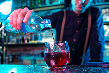 Image showing Close up of barman decorating, preparing of alcoholic cold cocktail in multicolored neon light