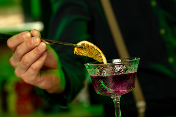 Image showing Close up of barman finishes preparation of alcoholic cocktail in multicolored neon light