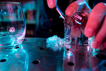 Image showing Close up of barman crushing a big piece of ice on the bar counter with a special bar equipment on it for a cocktail