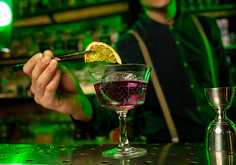 Image showing Close up of barman finishes preparation of alcoholic cocktail in multicolored neon light