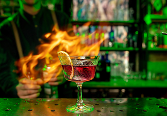 Image showing Close up of alcoholic cocktail, beverage, drink in multicolored neon light with fire flames on the background