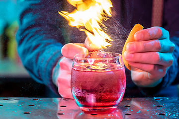 Image showing Close up of alcoholic cocktail, beverage, drink in multicolored neon light with fire flames setting on orange\'s spraying juice