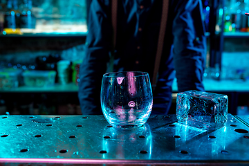 Image showing Close up of huge ice cube and drinking glass in multicolored neon light at bar