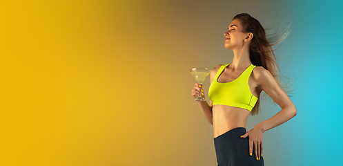 Image showing Fashion portrait of young fit and sportive woman drinking cocktail on gradient background. Perfect body ready for summertime. Flyer with copyspace.