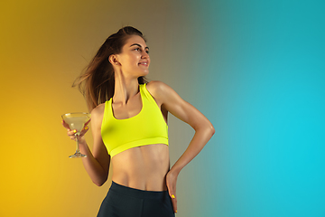 Image showing Fashion portrait of young fit and sportive woman drinking cocktail on gradient background. Perfect body ready for summertime.